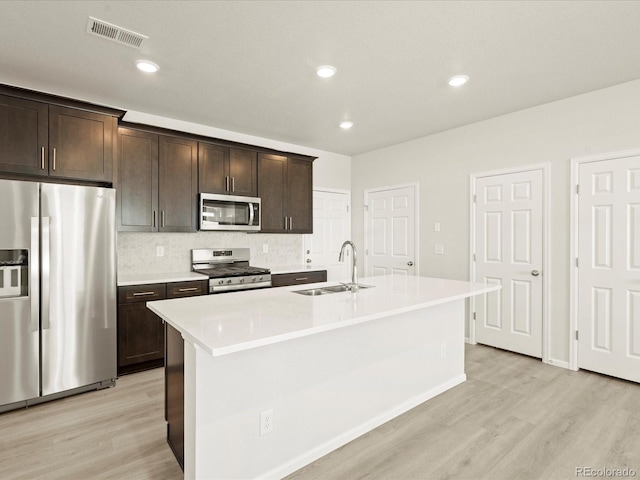 kitchen with appliances with stainless steel finishes, sink, a kitchen island with sink, dark brown cabinetry, and light wood-type flooring