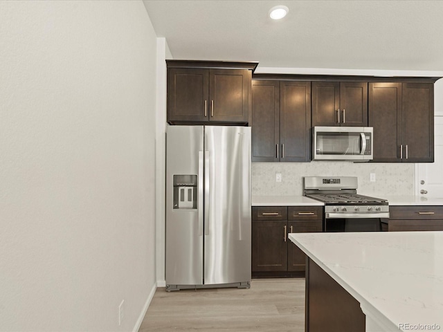 kitchen with light stone countertops, appliances with stainless steel finishes, dark brown cabinetry, and light hardwood / wood-style flooring