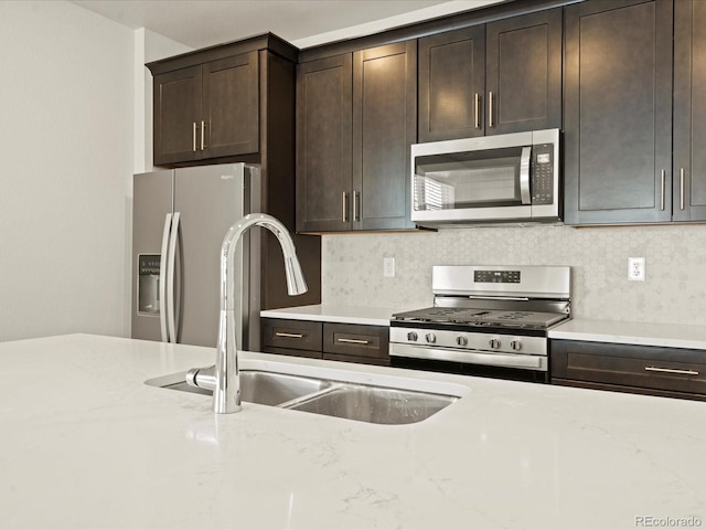 kitchen with sink, appliances with stainless steel finishes, dark brown cabinets, light stone countertops, and decorative backsplash