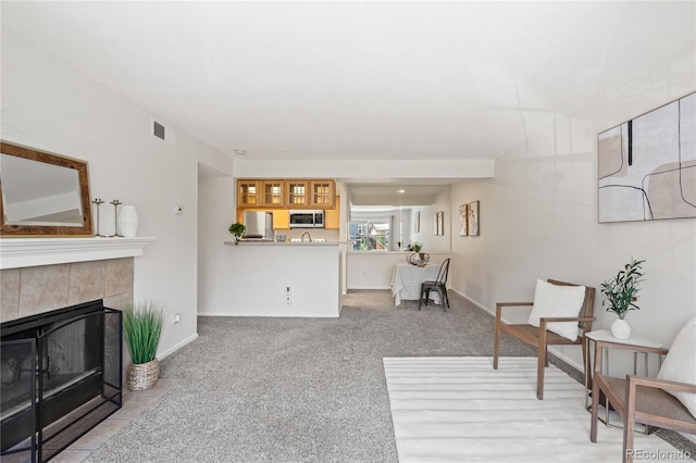 living area featuring a tiled fireplace, light carpet, and baseboards