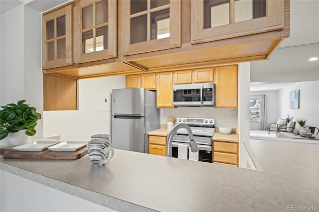 kitchen featuring appliances with stainless steel finishes, light brown cabinets, glass insert cabinets, light countertops, and a sink