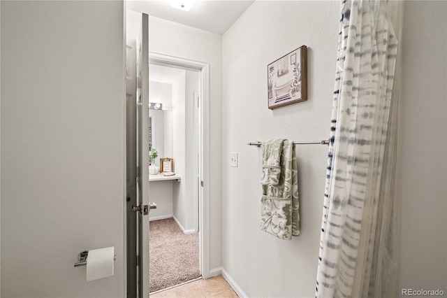 hall featuring baseboards, tile patterned floors, and carpet flooring