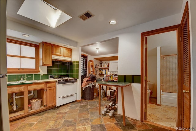 6805 Marshmerry Ln, Evergreen, CO 80439 - kitchen with white range with gas cooktop, decorative backsplash, stone finish floors, under cabinet range hood, and recessed lighting
