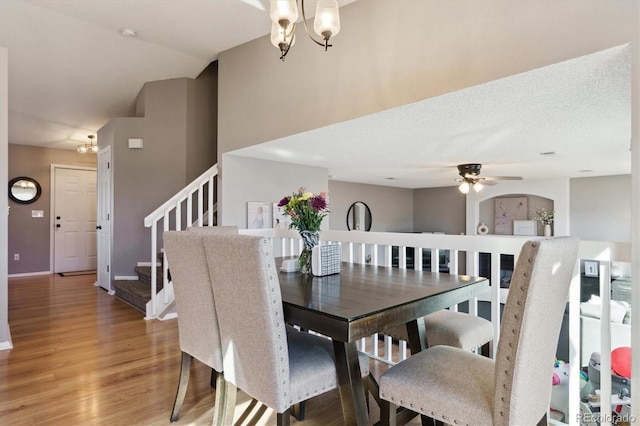 dining area featuring ceiling fan with notable chandelier, a textured ceiling, light wood-type flooring, baseboards, and stairs