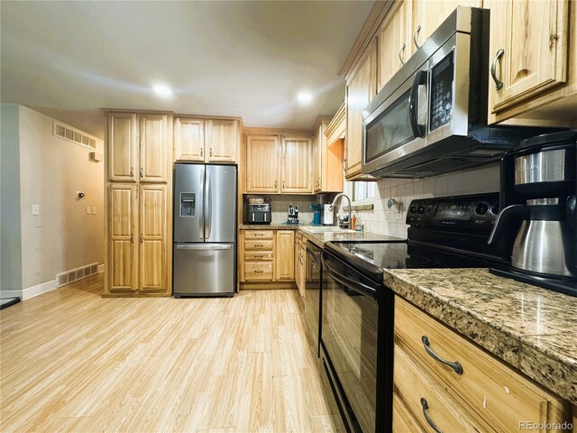 kitchen featuring light brown cabinets, light wood-style flooring, decorative backsplash, visible vents, and black appliances