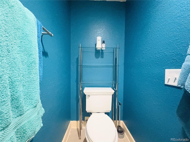 bathroom featuring baseboards, a textured wall, and toilet