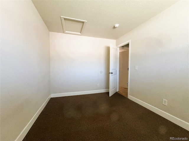 spare room with baseboards, attic access, and dark carpet