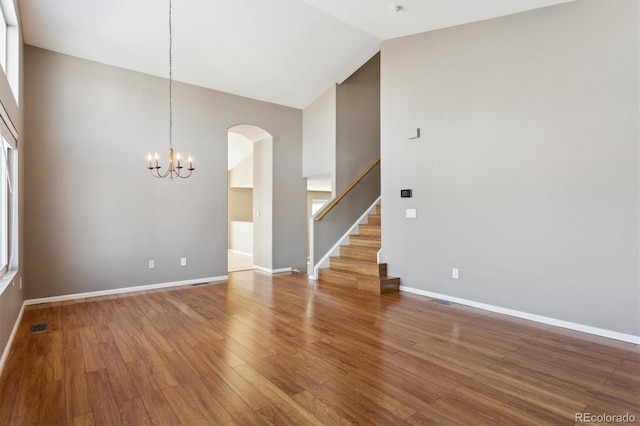 empty room featuring wood-type flooring, a chandelier, and high vaulted ceiling