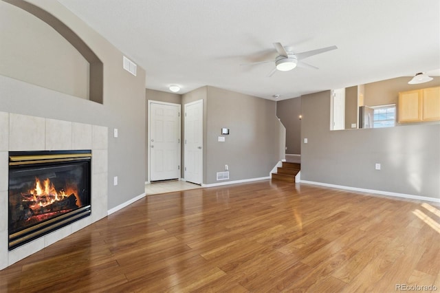 unfurnished living room featuring a tiled fireplace, ceiling fan, and light hardwood / wood-style floors