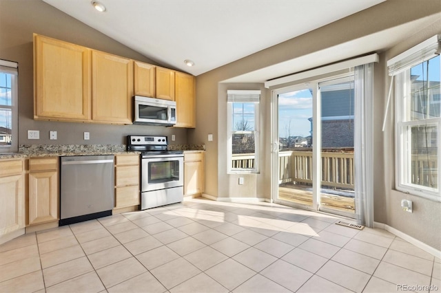 kitchen with lofted ceiling, light stone counters, stainless steel appliances, and light brown cabinets