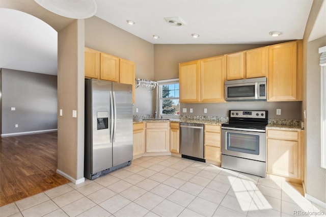 kitchen featuring light tile patterned flooring, light stone counters, vaulted ceiling, light brown cabinets, and stainless steel appliances