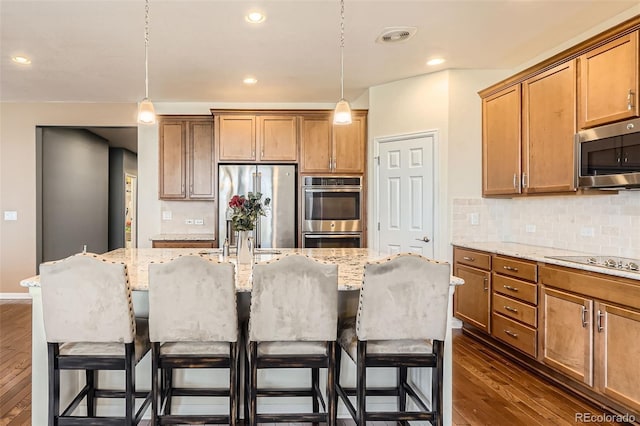 25561 E 5th Pl, Aurora, CO 80018 - kitchen with appliances with stainless steel finishes, dark wood-style flooring, decorative backsplash, a kitchen island with sink, and a kitchen breakfast bar