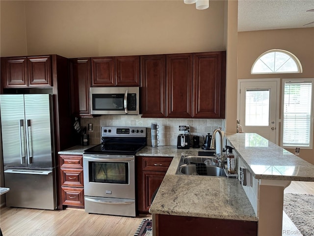 6887 S Dover Way, Littleton, CO 80128 - kitchen featuring appliances with stainless steel finishes, a sink, a peninsula, tasteful backsplash, and light wood-style flooring