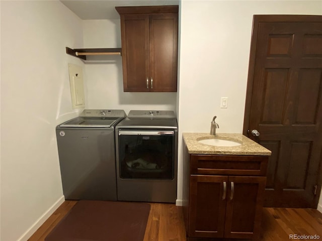 laundry area featuring electric panel, sink, cabinets, washer and dryer, and dark wood-type flooring