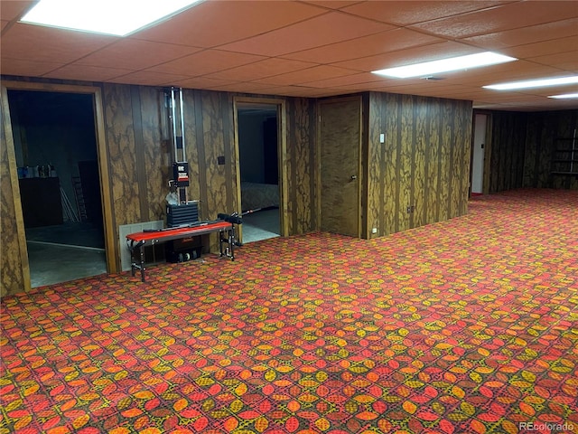 basement featuring wood walls, a drop ceiling, and carpet flooring