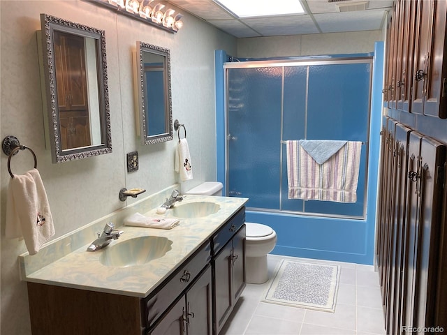 full bathroom with tile patterned flooring, bath / shower combo with glass door, a drop ceiling, toilet, and dual vanity