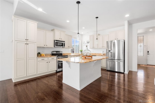 kitchen with a kitchen bar, light stone counters, dark wood-style floors, a center island, and appliances with stainless steel finishes