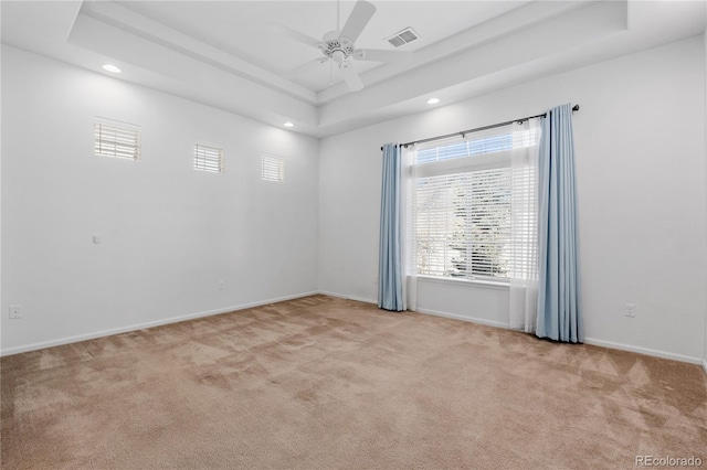 empty room featuring light carpet, visible vents, a raised ceiling, and baseboards