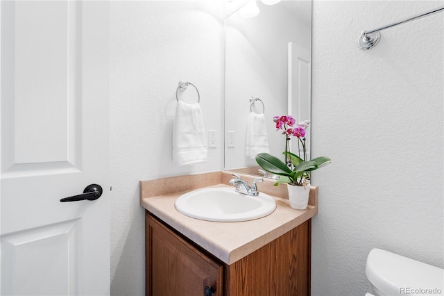 half bath with vanity, toilet, and a textured wall