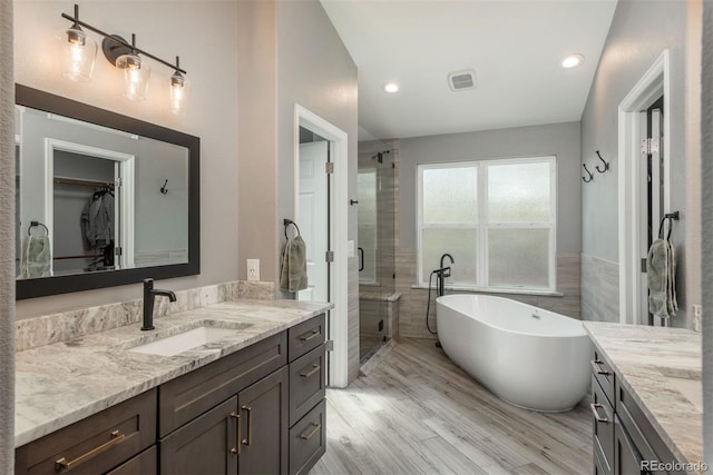bathroom featuring vanity, a shower stall, a freestanding tub, wood finished floors, and a spacious closet