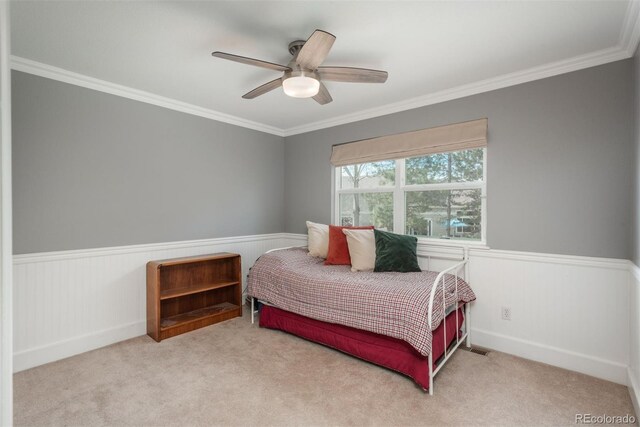 carpeted bedroom featuring wainscoting, crown molding, and a ceiling fan