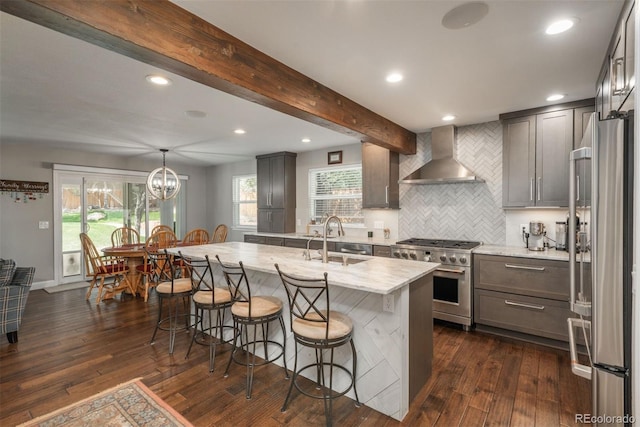 kitchen with high quality appliances, wall chimney exhaust hood, a kitchen breakfast bar, a sink, and dark wood-style flooring