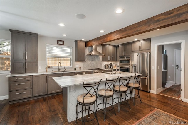 kitchen with appliances with stainless steel finishes, wall chimney exhaust hood, a sink, dark wood-style flooring, and a kitchen breakfast bar