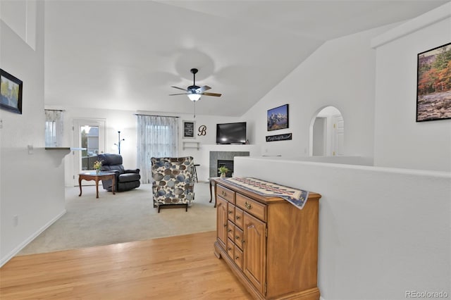 12454 Tex Tan Rd, Peyton, CO 80831 - living room with vaulted ceiling, ceiling fan, a tiled fireplace, light wood finished floors, and light carpet