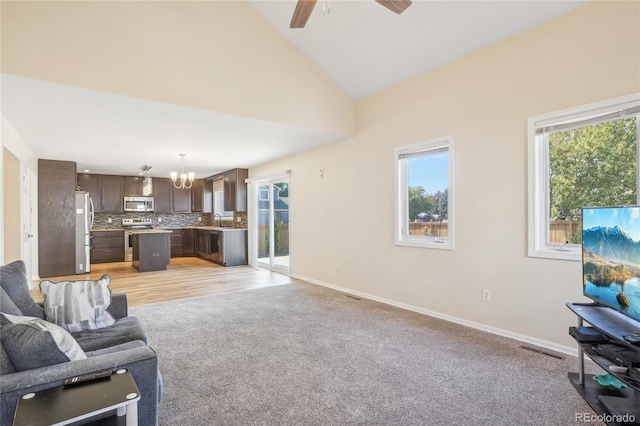 living room featuring light colored carpet, high vaulted ceiling, sink, and ceiling fan with notable chandelier