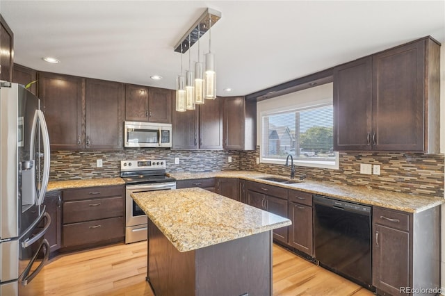 kitchen with sink, decorative light fixtures, a center island, appliances with stainless steel finishes, and light stone countertops