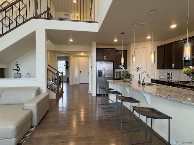 kitchen featuring light stone countertops, stainless steel fridge with ice dispenser, hanging light fixtures, dark brown cabinets, and sink