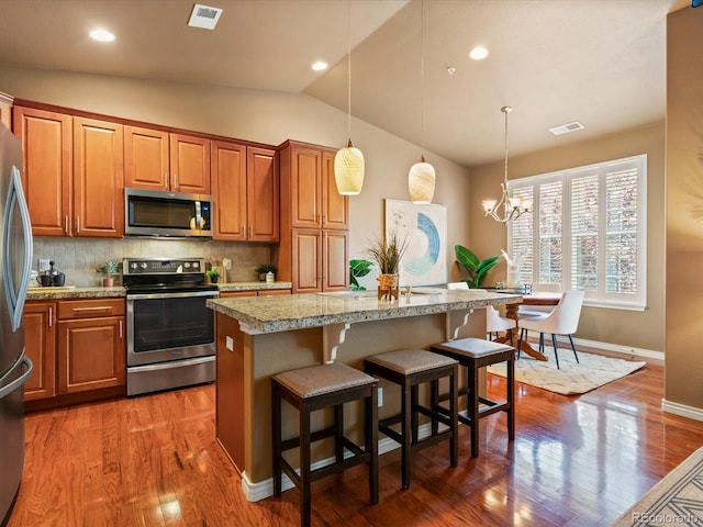 11962 W Long Cir Unit 203, Littleton, CO 80127 - kitchen featuring stainless steel appliances, a kitchen island, vaulted ceiling, brown cabinets, and decorative backsplash