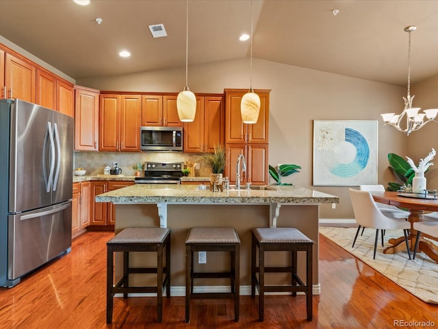 11962 W Long Cir Unit 203, Littleton, CO 80127 - kitchen with stainless steel appliances, a chandelier, vaulted ceiling, tasteful backsplash, and light wood-style flooring