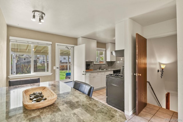 kitchen with wall chimney exhaust hood, light tile patterned floors, white cabinetry, and range with gas cooktop