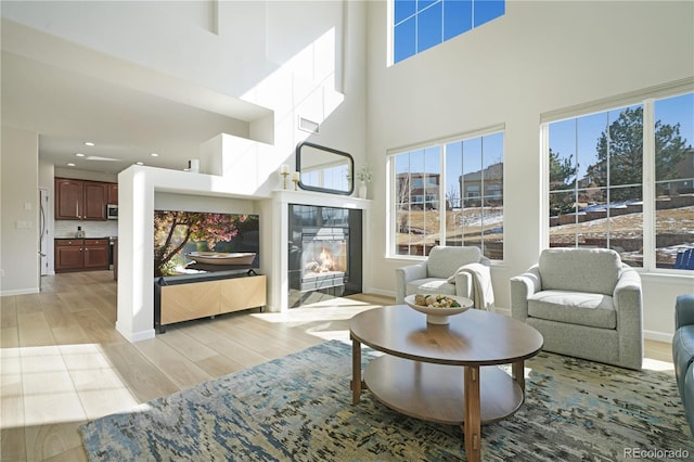 living area featuring a high ceiling, light wood-type flooring, a tile fireplace, and a healthy amount of sunlight