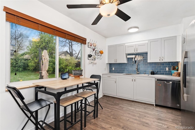 kitchen featuring appliances with stainless steel finishes, a sink, backsplash, light countertops, and light wood-type flooring