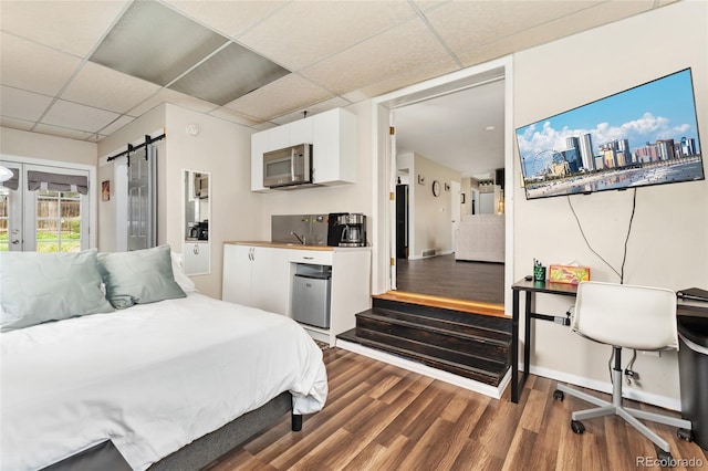 bedroom with a drop ceiling, wood finished floors, and a barn door