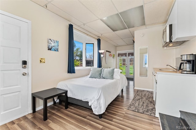 bedroom featuring a paneled ceiling, a sink, wood finished floors, french doors, and baseboards