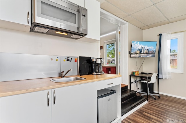 kitchen with stainless steel microwave, a sink, dark wood-type flooring, white cabinets, and light countertops