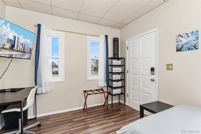 bedroom featuring a drop ceiling, wood finished floors, baseboards, and a desk