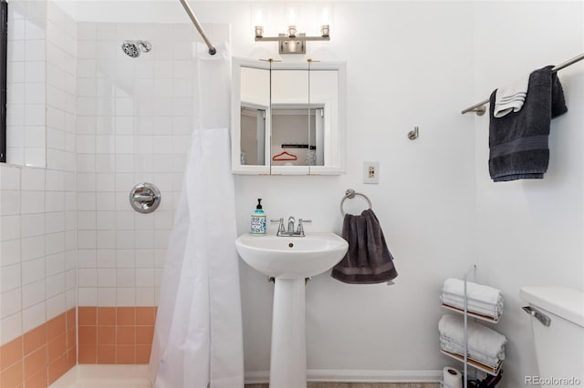 bathroom with a tile shower, toilet, and a sink