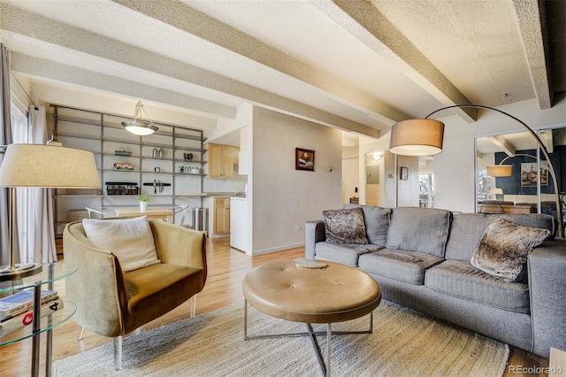 living room with baseboards, beamed ceiling, light wood-type flooring, and a textured ceiling