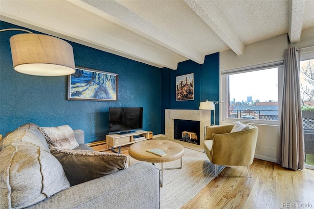 living room with wood finished floors, beam ceiling, baseboards, a textured ceiling, and a tile fireplace
