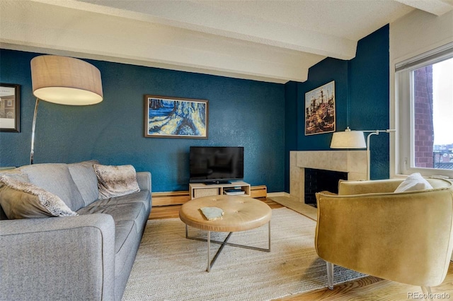living room featuring plenty of natural light, beamed ceiling, wood finished floors, and a tile fireplace