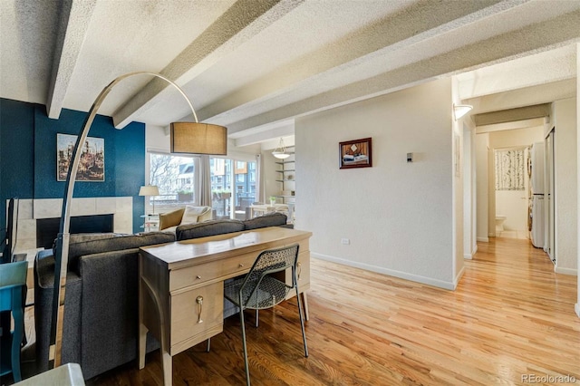 home office with a textured ceiling, baseboards, light wood-type flooring, and beam ceiling