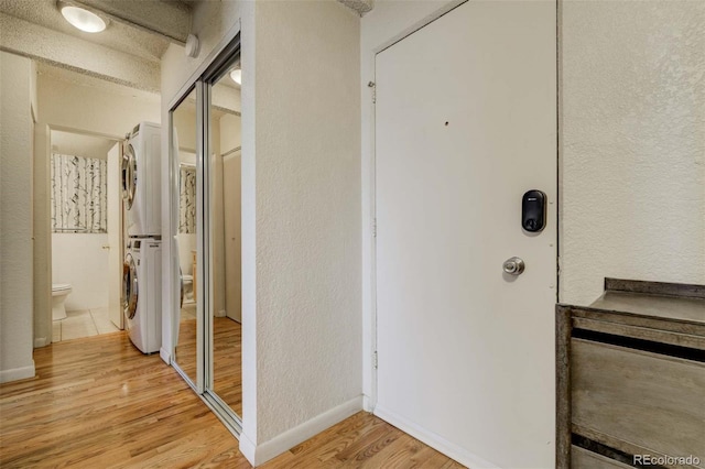 hallway with baseboards, a textured wall, light wood-type flooring, and stacked washer and dryer