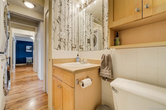 half bath featuring backsplash, wood finished floors, vanity, toilet, and stacked washer and clothes dryer