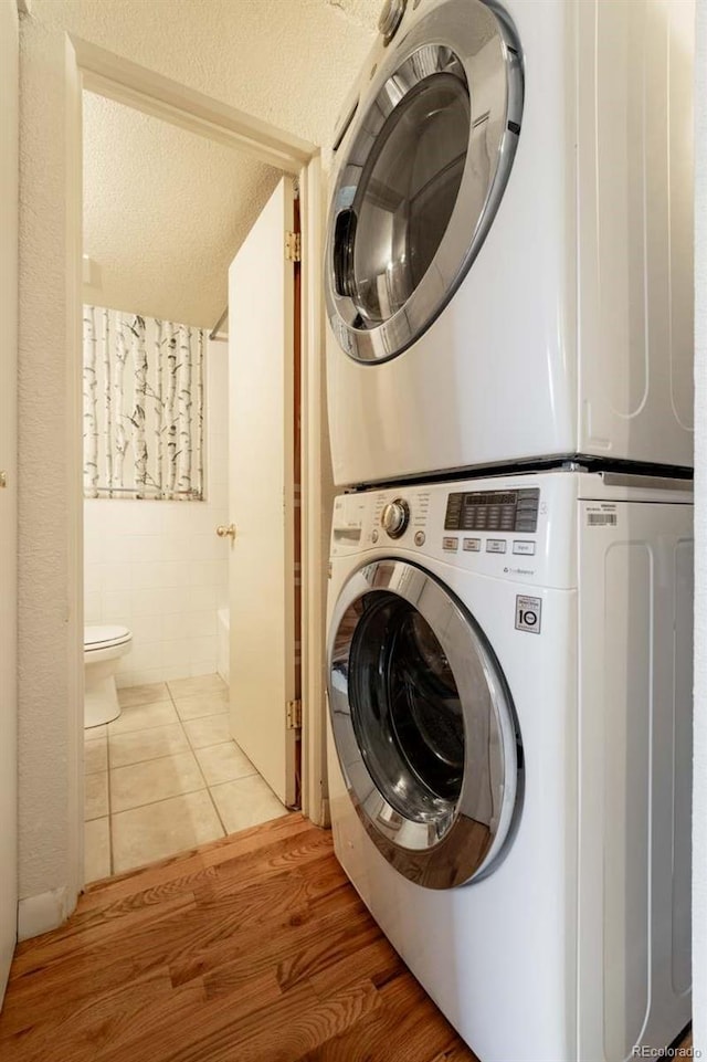 laundry room with stacked washer / drying machine, laundry area, tile patterned flooring, a textured ceiling, and tile walls