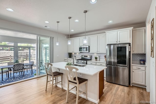 21837 E Stanford Cir, Aurora, CO 80015 - kitchen with appliances with stainless steel finishes, light wood-style floors, tasteful backsplash, a center island with sink, and light countertops