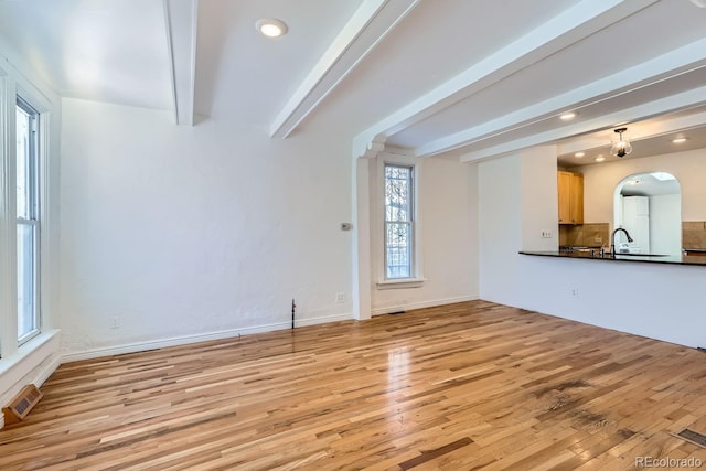 unfurnished living room with beam ceiling, light hardwood / wood-style floors, and sink